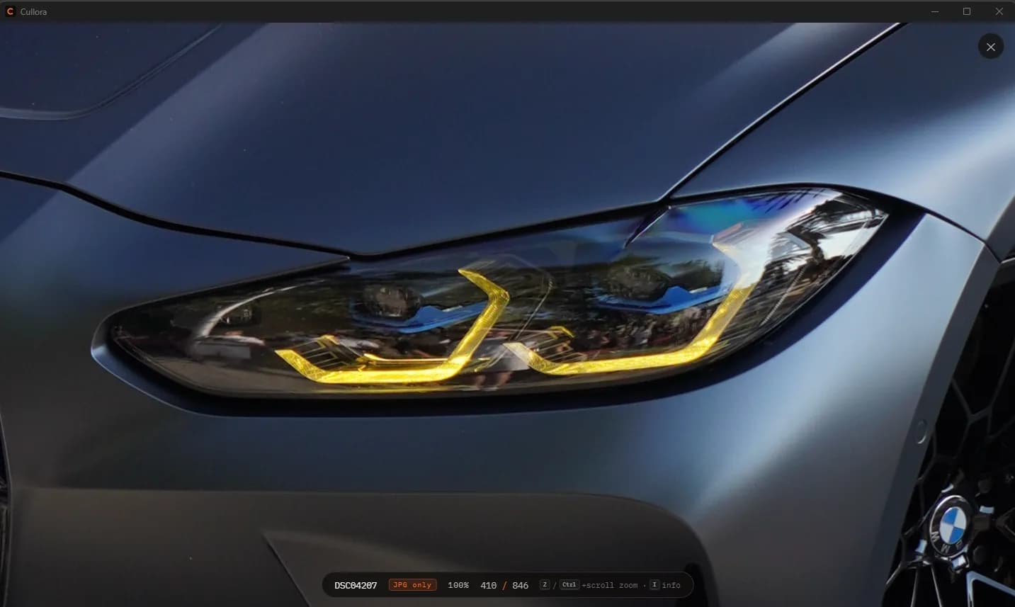 The viewer zoomed to 100% on a BMW headlight, filling the window, with the zoom level and frame position shown in the heads-up display along the bottom.